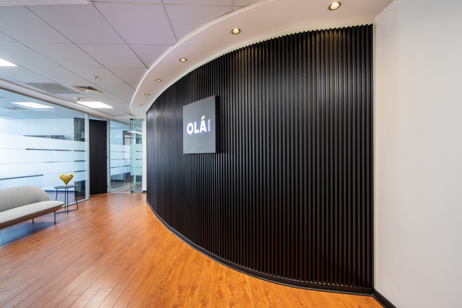 Recepción de las oficinas Olá Hotel con muro curvo de listones negros y letrero iluminado